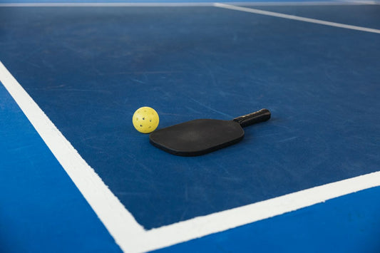 A pickleball paddle and ball resting on a blue court